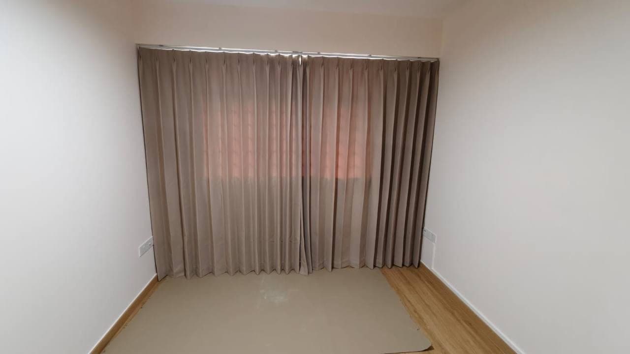 A taupe curtain drawn fully closed across a window in an empty room, daylight glowing through the fabric