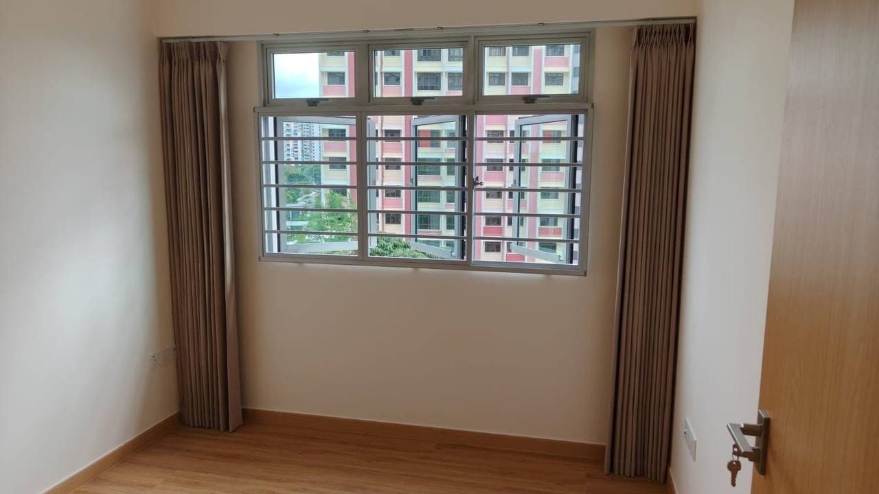 An empty room with taupe curtains gathered at both sides of a window, timber flooring and bare walls