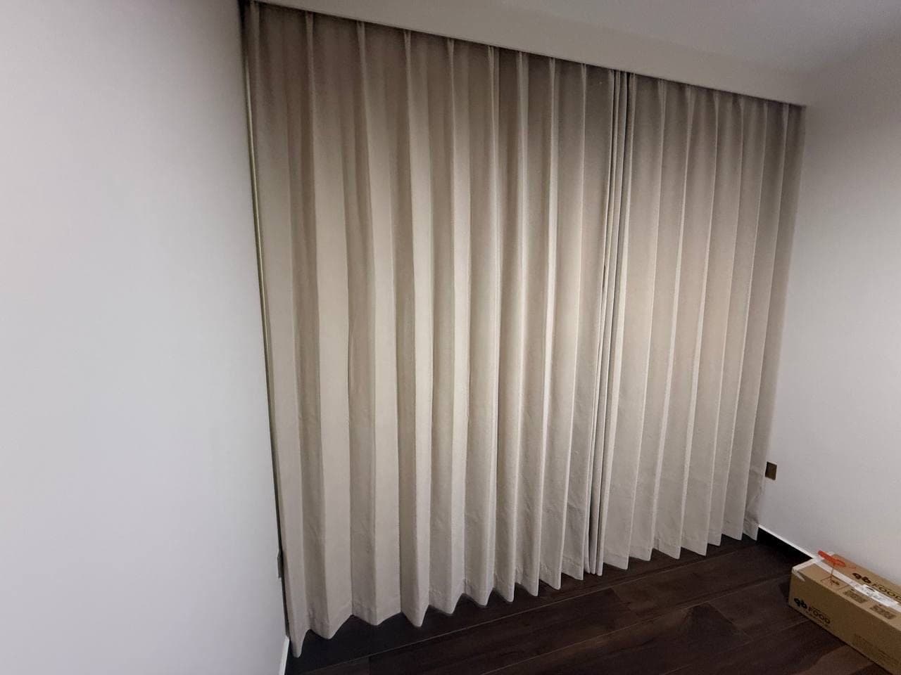 A taupe curtain closed across a window wall in a room with dark flooring