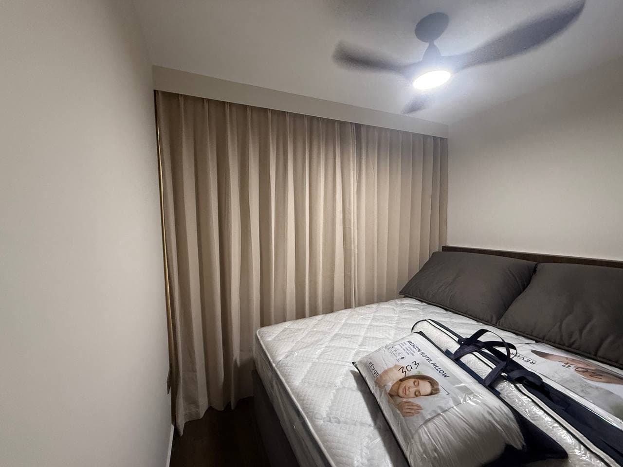 A bedroom with a white sheer drawn across the window and taupe curtains at the sides, bed in the foreground