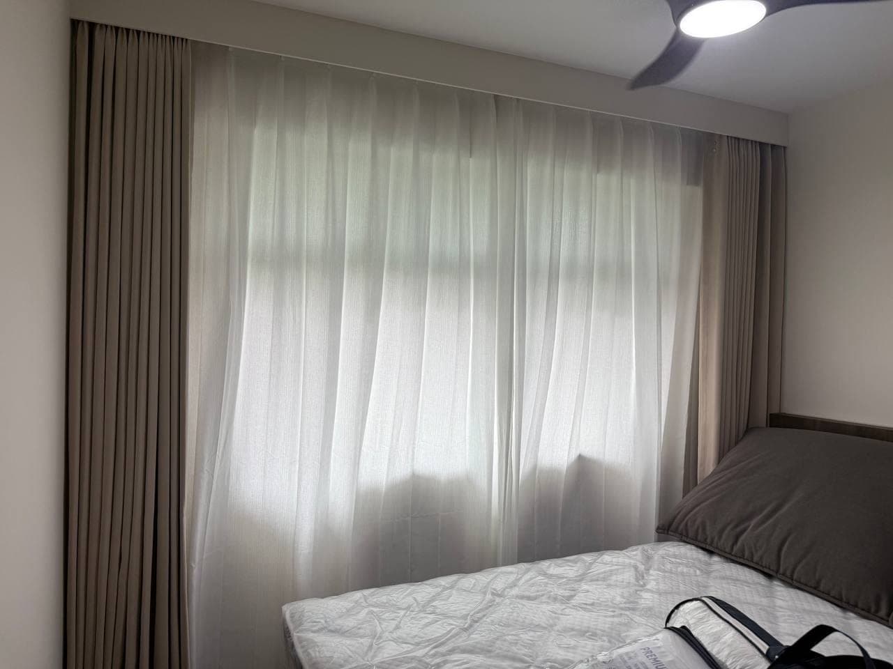 A bedroom with a taupe curtain closed across the window beside a wall-mounted television and an upholstered bed