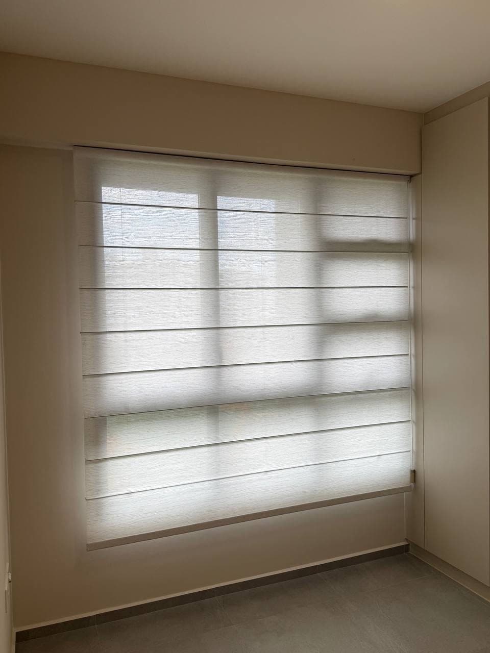 A fabric blind covering a window in horizontal bands of alternating opacity, fitted flush inside the reveal