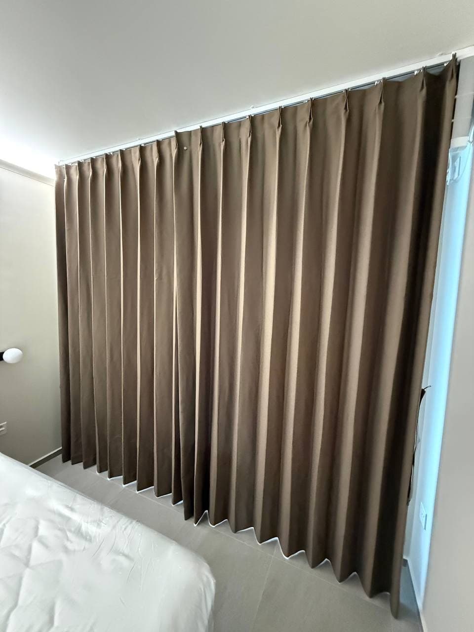 A brown curtain drawn across a bedroom window wall in even folds, bed visible at the lower edge
