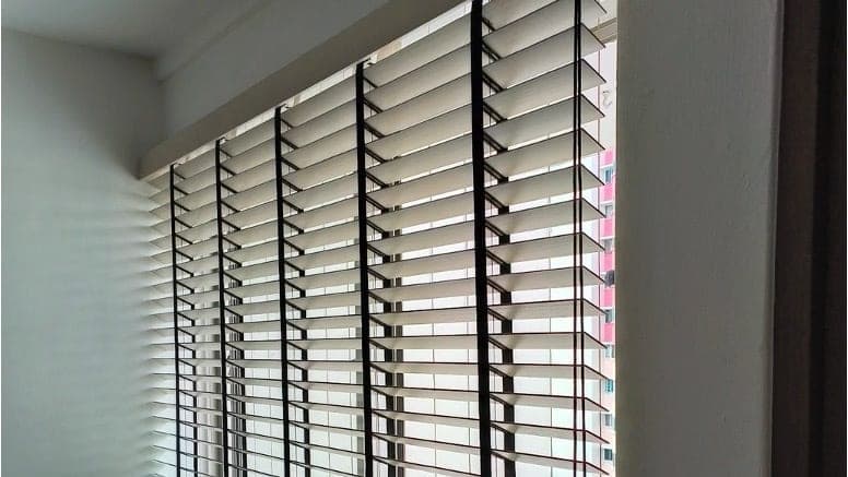 Aluminium Venetian blinds fitted to an HDB window, slats tilted to filter afternoon light