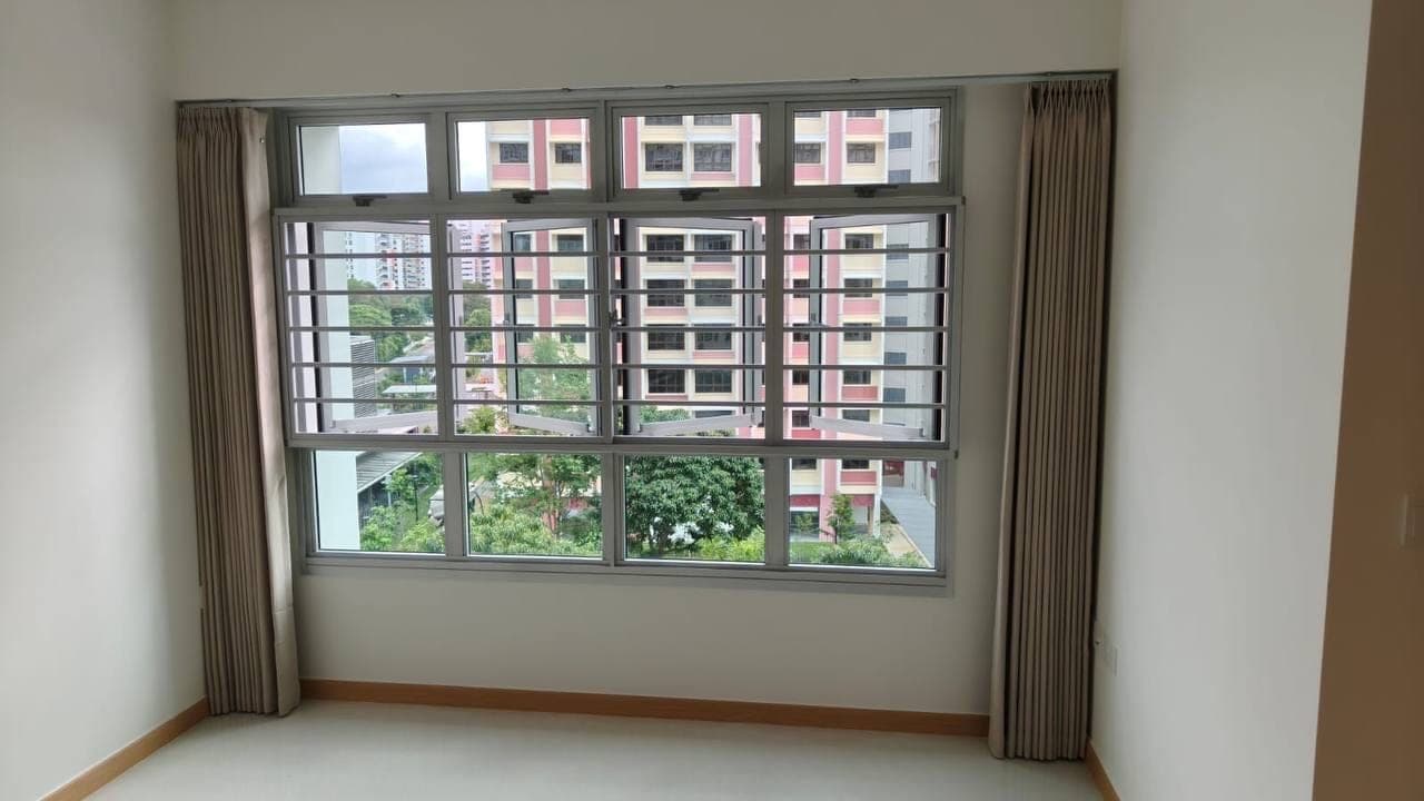 An empty flat with taupe curtains held open at both sides of an HDB window, neighbouring blocks visible outside