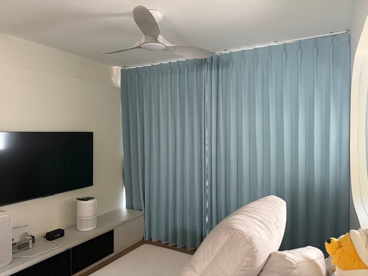 A living room with blue-grey curtains drawn across the window wall beside a wall-mounted television and a pale sofa